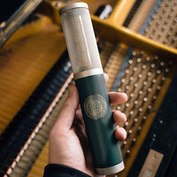 Front view of Pearl Microphone Labs ELM-T Single held in hand with piano background