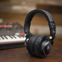Black headphones on a wooden surface with a blurred keyboard in the background