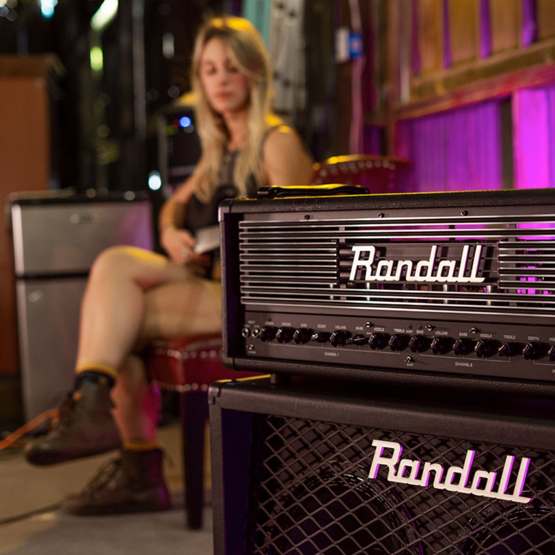 Angled view of Randall Thrasher Guitar Amplifier Head on top of speaker cabinet with guitarist in the background in studio