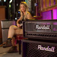 Angled view of Randall Thrasher Guitar Amplifier Head on top of speaker cabinet with guitarist in the background in studio