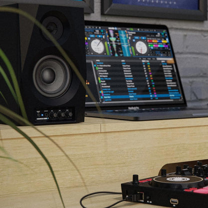 Angled view of Reloop DSM-3 BT Smart Desktop Monitor System w/ Wireless Input beside laptop and DJ controller on wooden desk