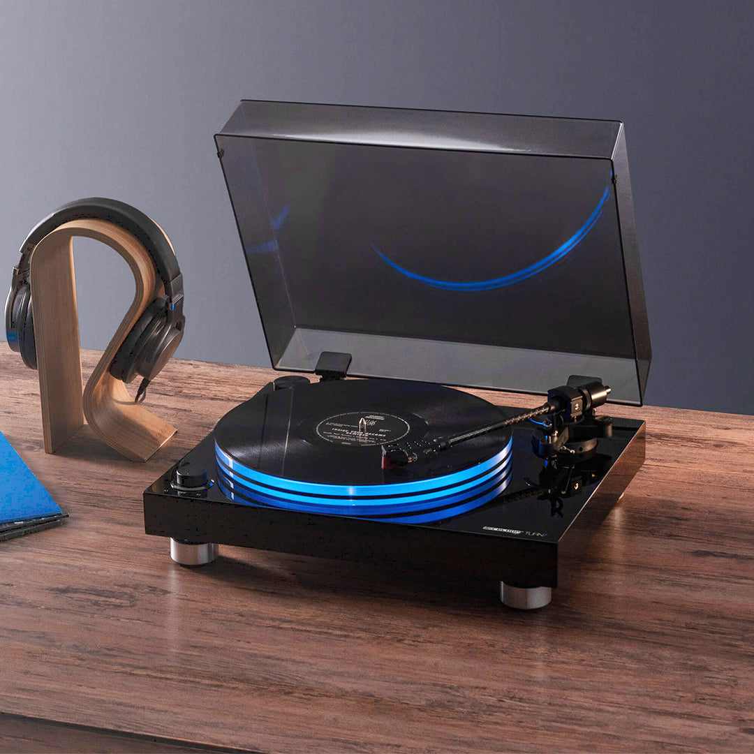 Angled front view of Reloop Turn 7 Premium Belt Drive USB Turntable System with headphones beside it on top of wooden surface with grey background
