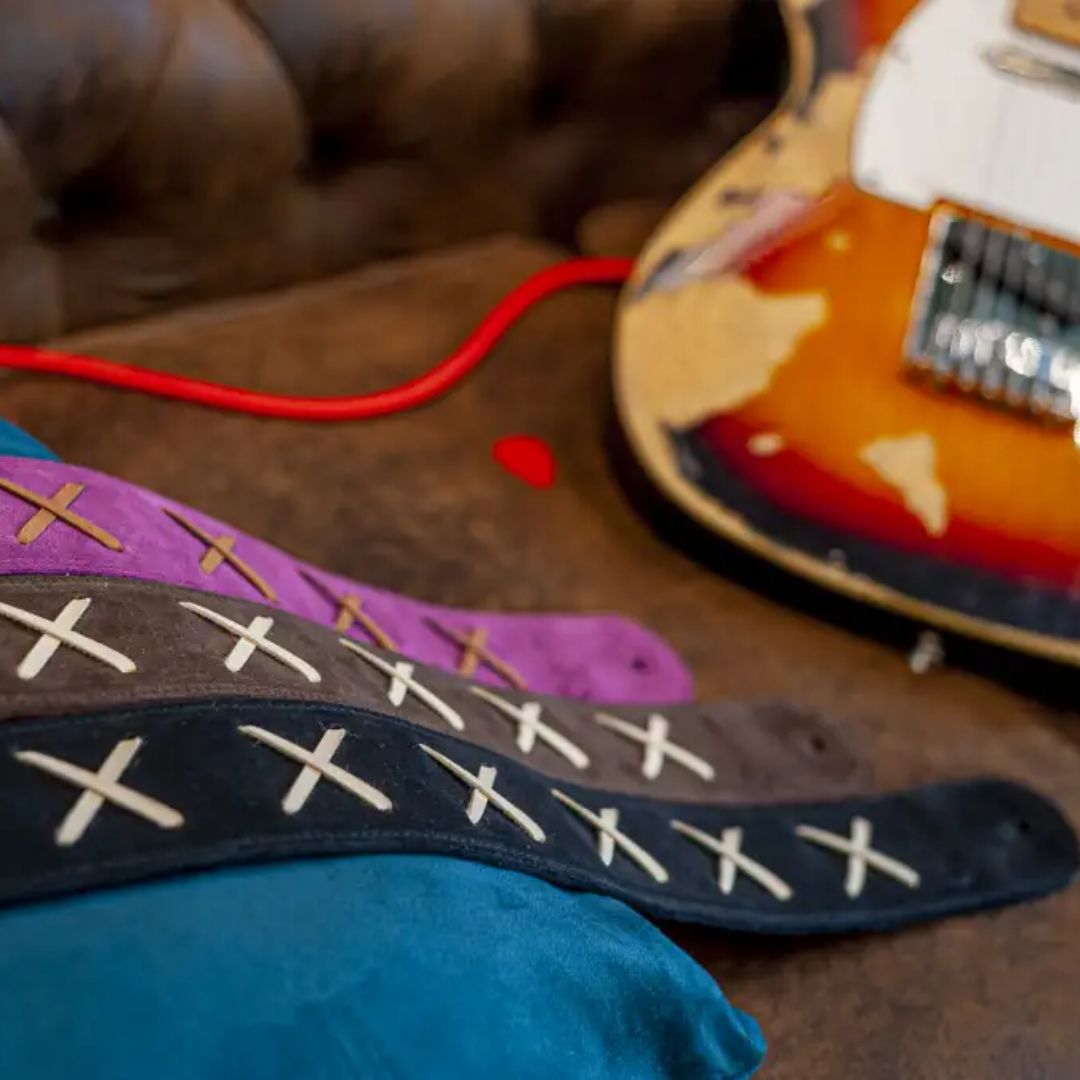 Collection of RightOn Legend D.G. Guitar Strap Purple, Brown, and Black laid on a brown couch with a guitar in the background