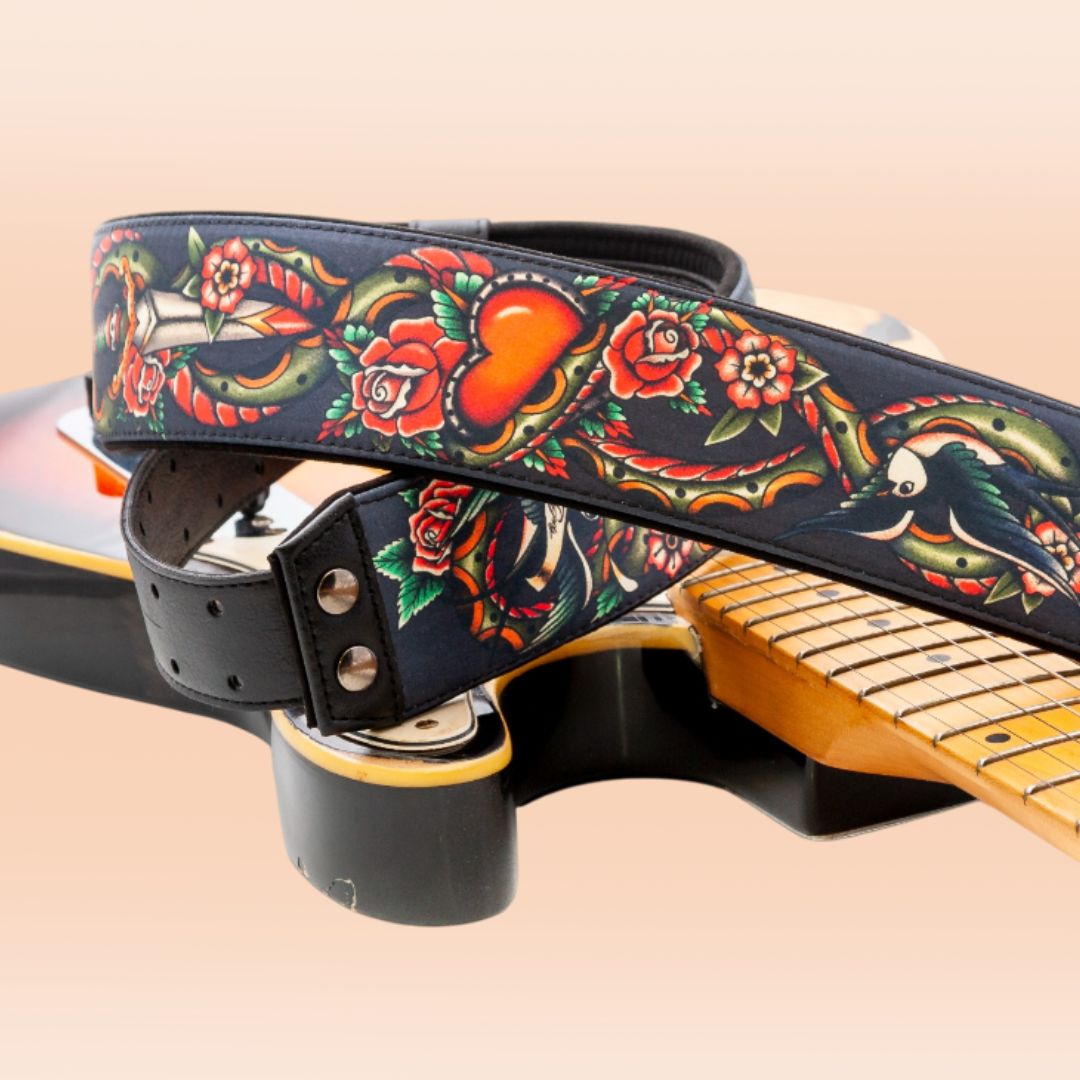 Close up view of RightOn Tattoo Guitar Strap on top of guitar on peach background