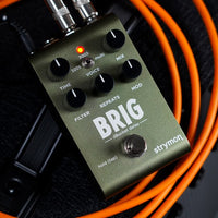 Angled front view of Strymon Brig on top of orange cables and amplifier