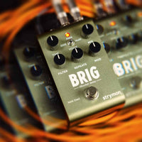 Angled front view through kaleidoscopic lens of Strymon Brig on top of orange cables with a dark background
