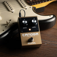 Strymon Canoga Vintage Silicon Fuzz Pedal leaning on guitar on top of wooden surface