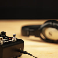 Strymon Iridium connected to headphones on wooden desk with black background