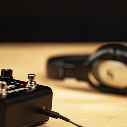 Strymon Iridium connected to headphones on wooden desk with black background