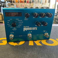 Front view of Strymon Mobius on top of black and yellow surface with guitars in background