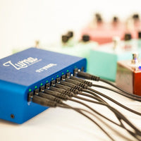 Angled view of Strymon Zuma with pedals plugged in on white background