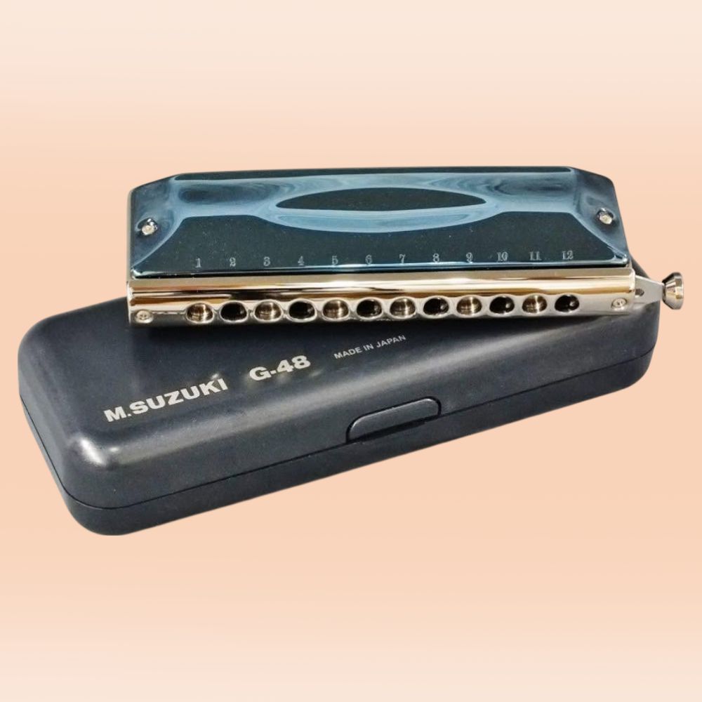 Front view of Suzuki G-48 Chromatic Gregoire Maret Signature Harmonica resting on top of its carrying case on orange background