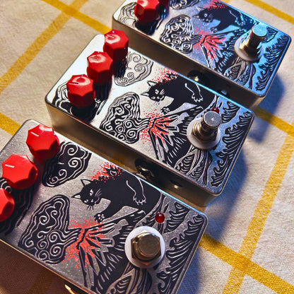 Angled view of multiple TONECAT CatZilla Drive Pedals on beige cloth with yellow stripes