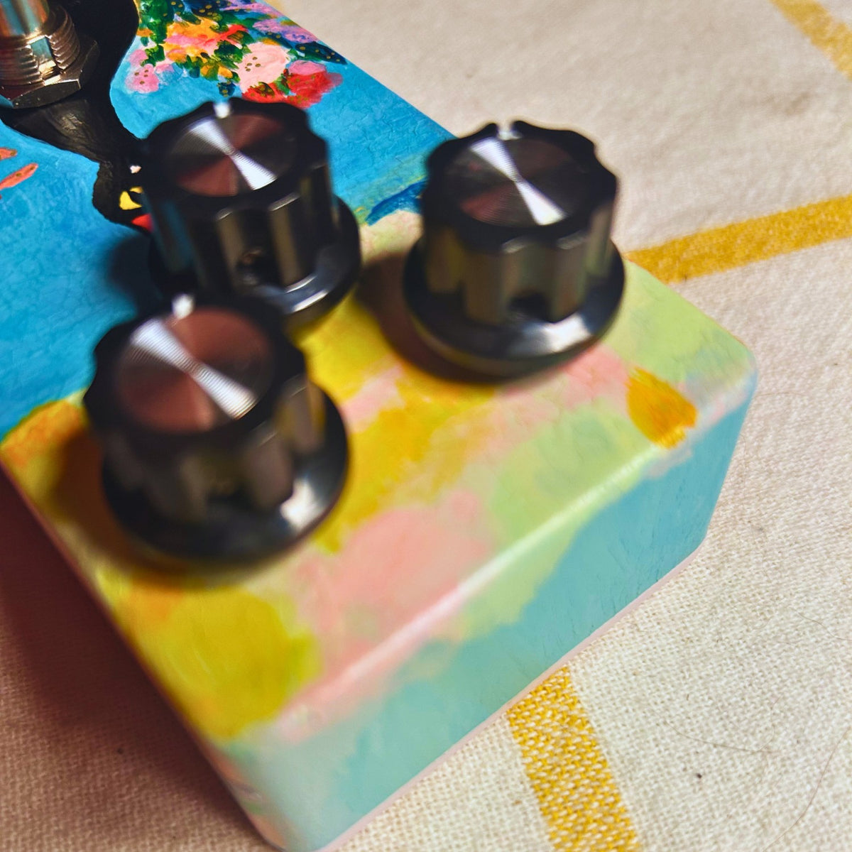 Angled close up view of TONECAT Cat au Fenêtre Delay Pedal on beige cloth with yellow stripes
