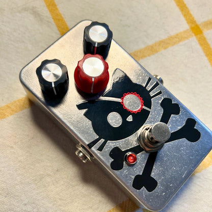 Angled view of TONECAT Cutthroat Kitty Distortion Pedal on beige cloth with yellow stripes