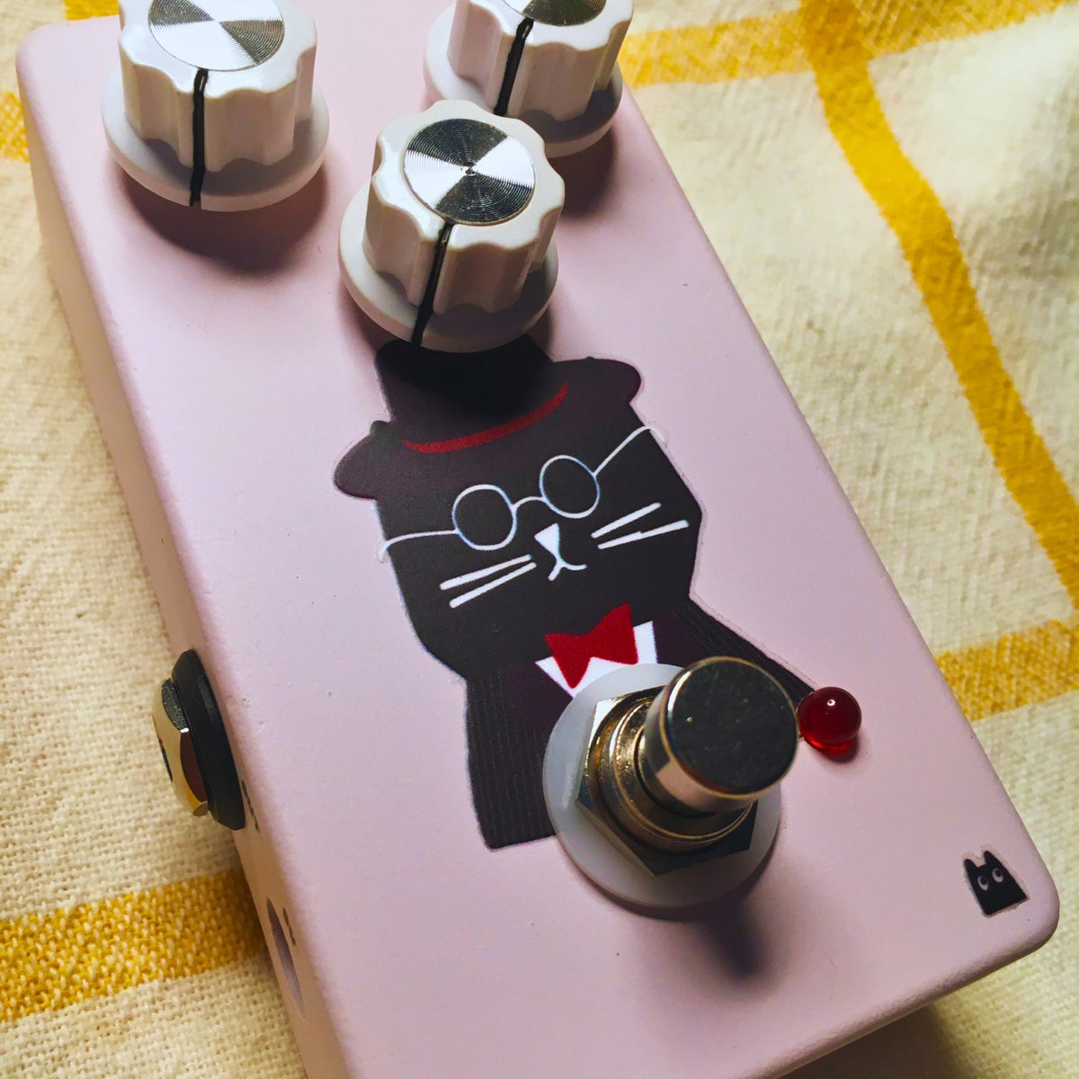 Close up angled view of TONECAT Hugo Overdrive Pedal on beige cloth with yellow stripes