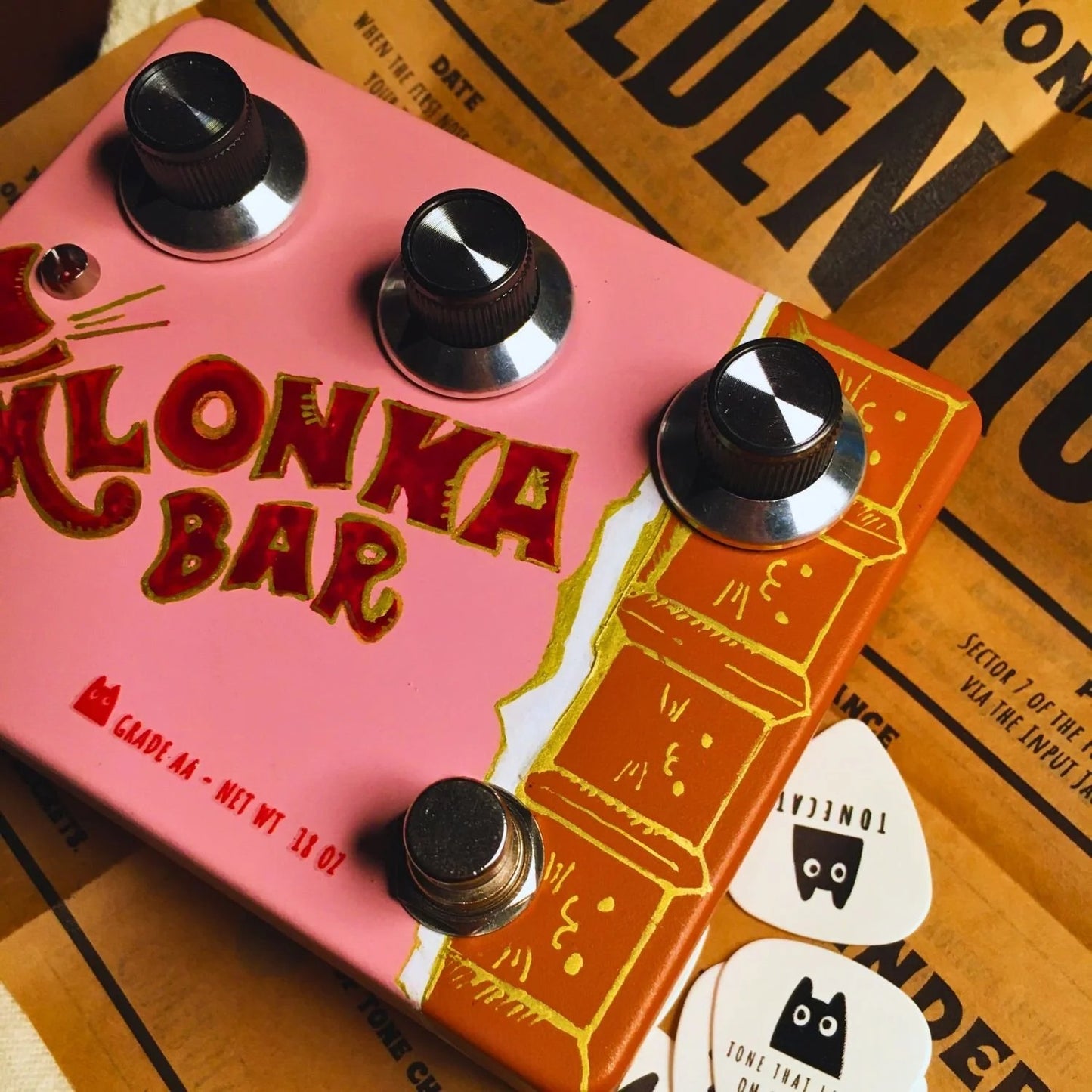 Close up angled view of TONECAT Klonka Bar Overdrive Pedal on included Golden Ticket manual with TONECAT picks around it