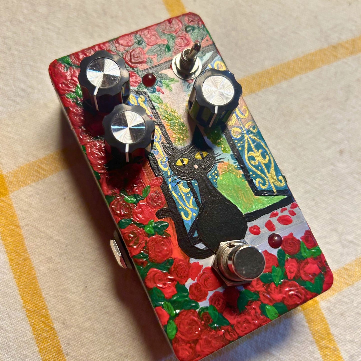 Angled view of TONECAT La Floraison Distortion Pedal on beige cloth with yellow stripes