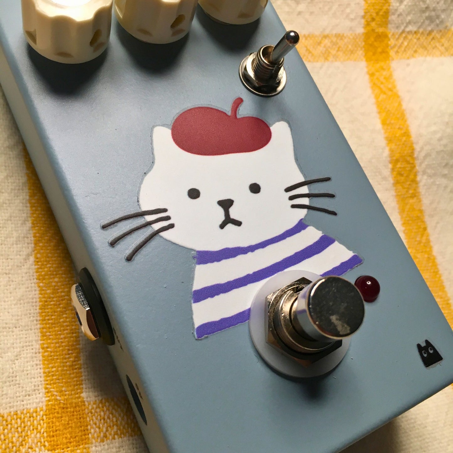 Close up angled view of TONECAT Luna Overdrive Pedal on beige cloth with yellow stripes