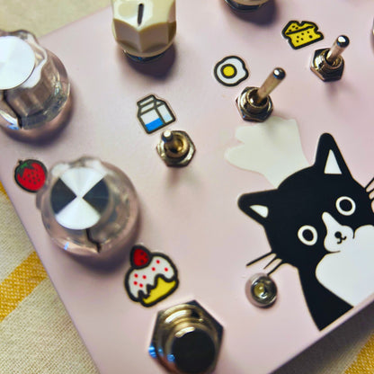 Close up angled view of TONECAT Meow A Deux Dual Channel Overdrive Pedal on beige cloth with yellow stripes
