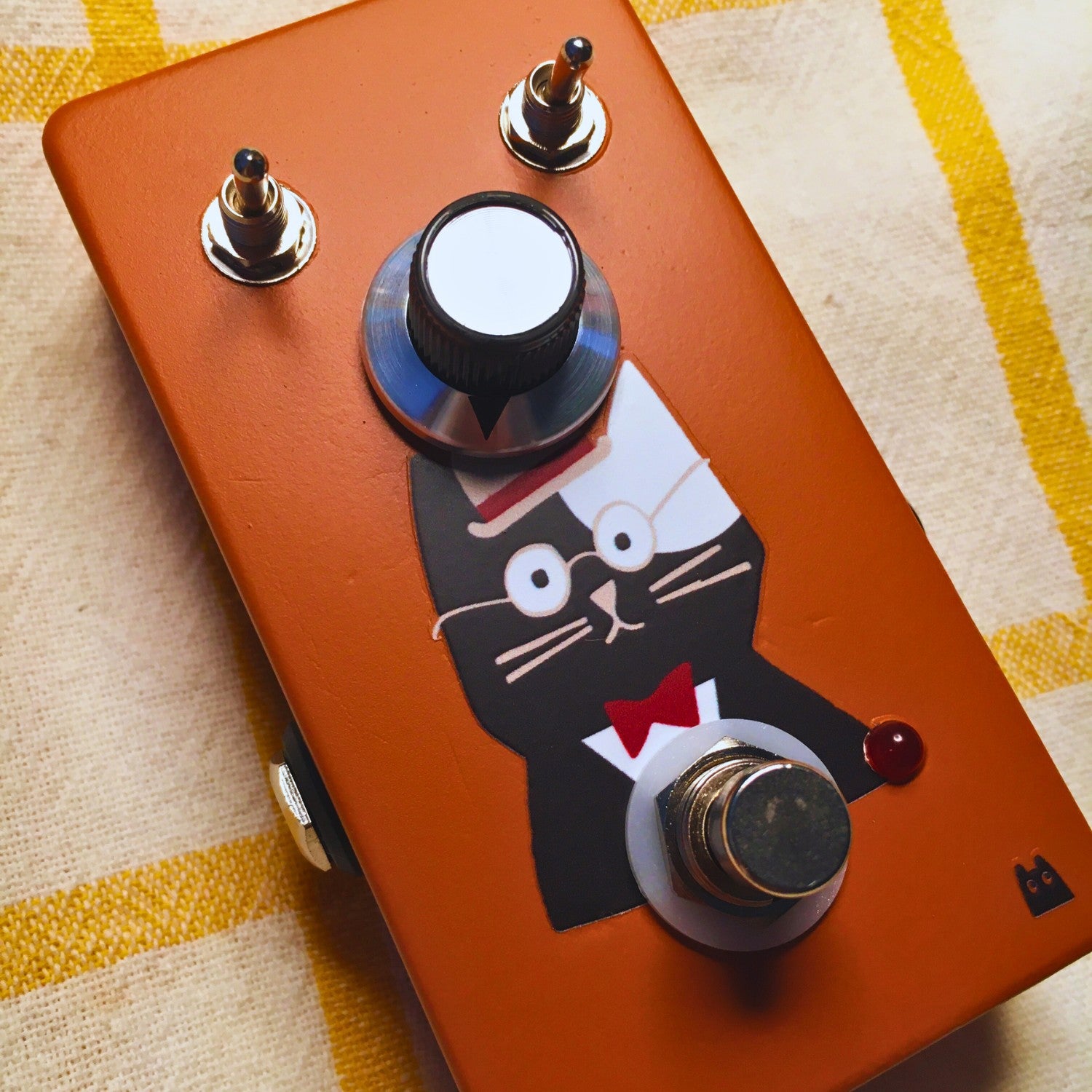 Angled close up view of TONECAT Papa Booster Pedal on beige cloth with yellow stripes