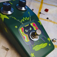 Close up angled view of TONECAT RadioCat Fuzz Bender Pedal on beige cloth with yellow stripes and multiple transistors scattered around it