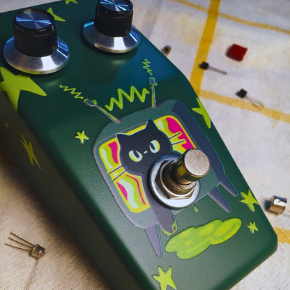 Close up angled view of TONECAT RadioCat Fuzz Bender Pedal on beige cloth with yellow stripes and multiple transistors scattered around it