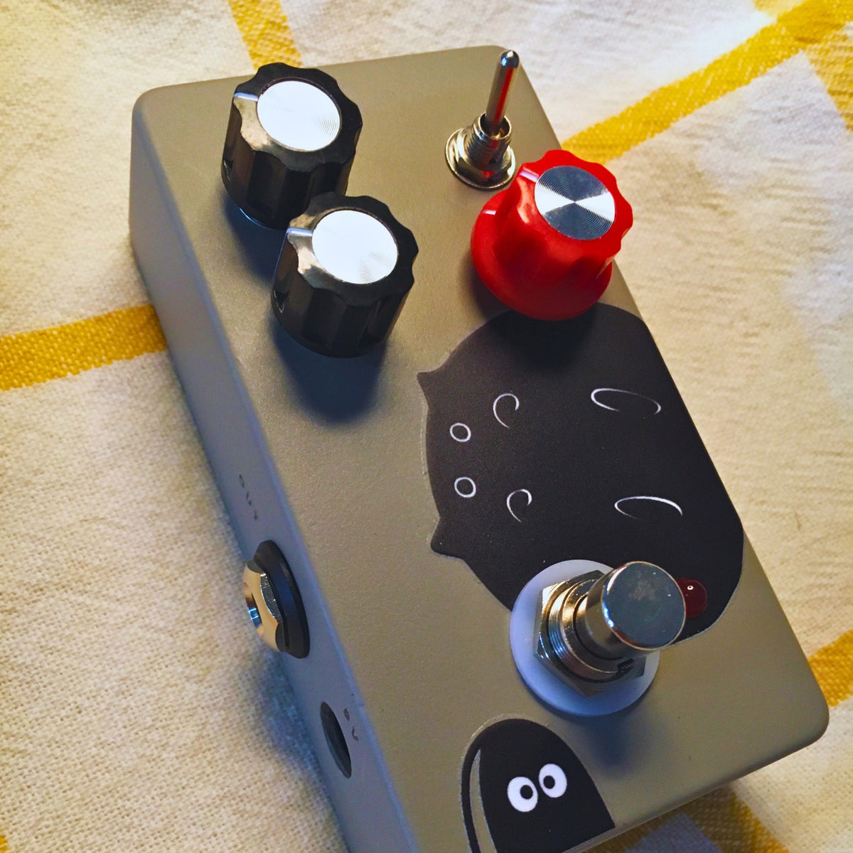 Close up angled view of TONECAT Rat Trap Distortion V2 Pedal on beige cloth with yellow stripes