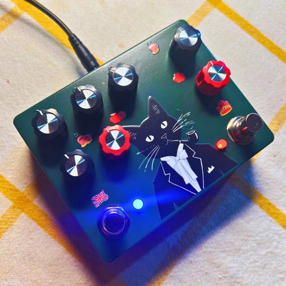 Angled view of TONECAT Sir Fuzzington Dual Drive & Fuzz Pedal with power cable attached to it on beige cloth with yellow stripes