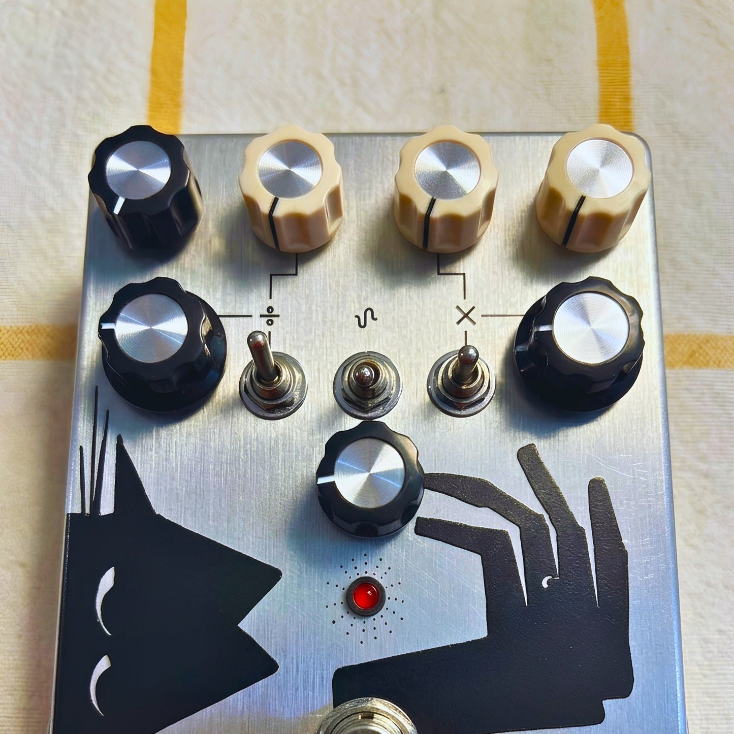 Close up front view of TONECAT Vanishing Tail Analogue PLL Synth Fuzz Pedal on beige cloth with yellow stripes