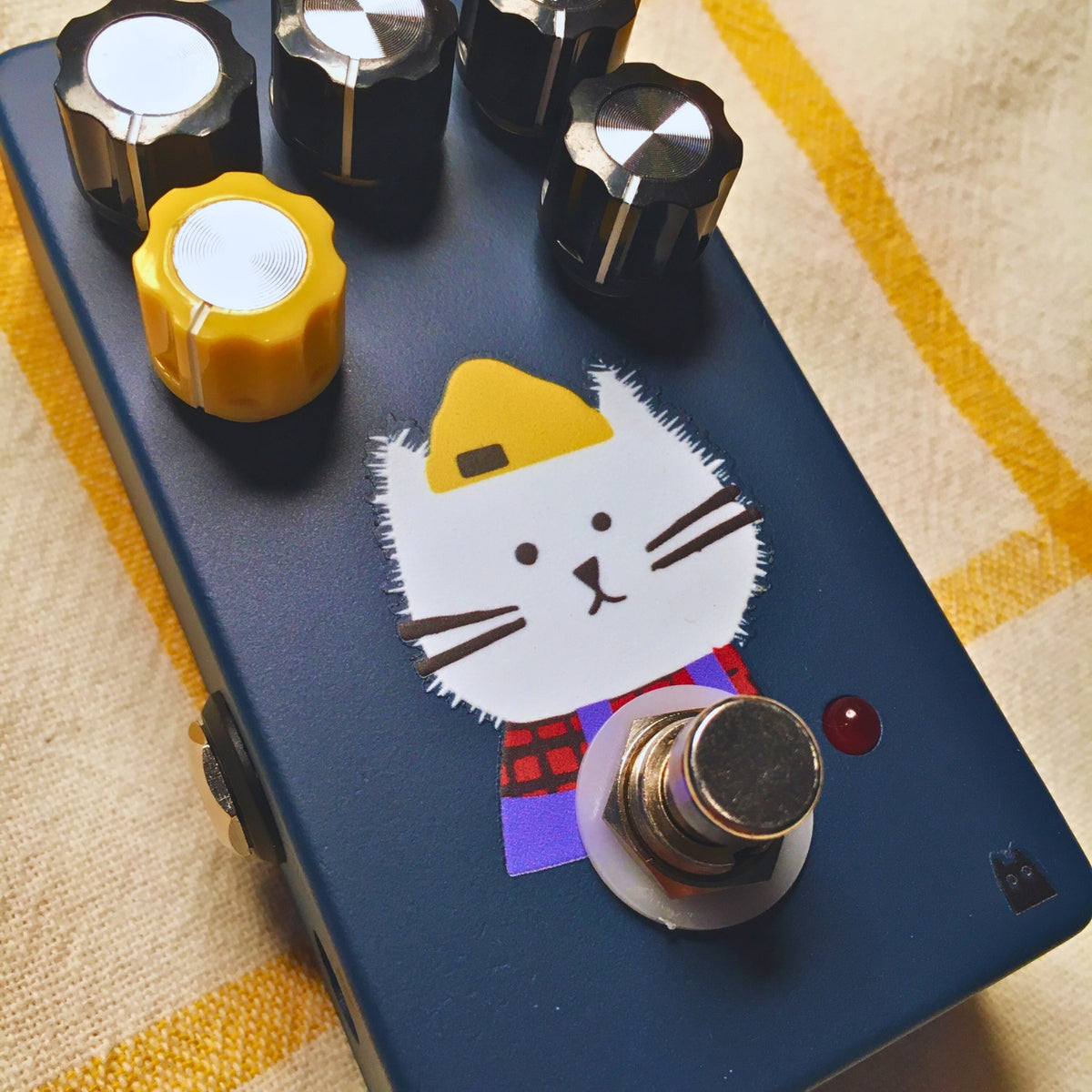 Angled close up view of TONECAT Ziggy Fuzz Pedal on beige cloth with yellow stripes