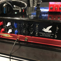 Close up of black rackmount effect on top of red microphone preamplifier on top of desk with headphones and red DI box