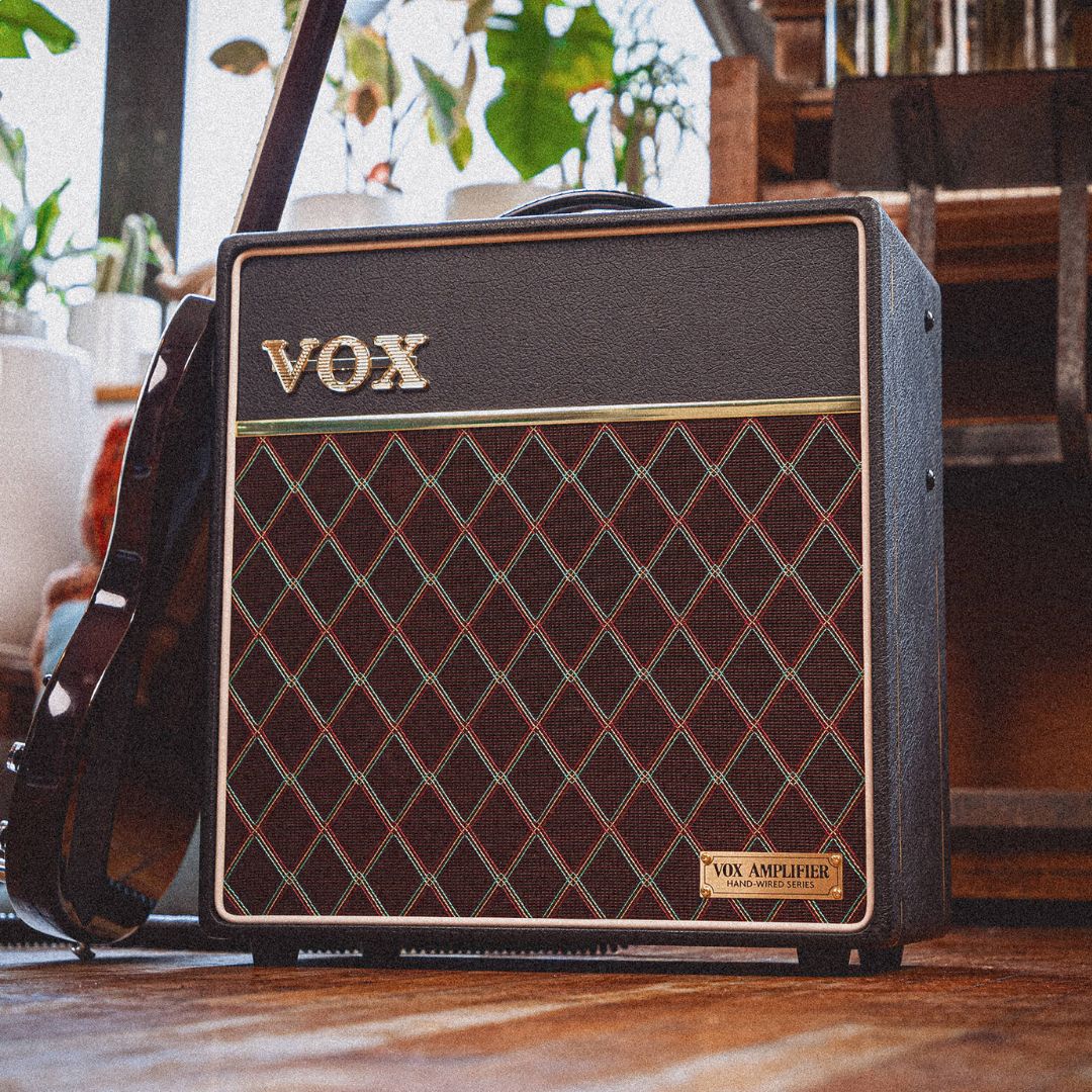 Angled front view of Vox AC4 Hand-Wired Guitar Amplifier with guitar leaning on it in living room
