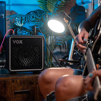 Vox MINI GO 10 Portable Modeling Guitar Amplifier on wooden surface with guitarist playing in the foreground in living room