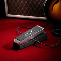 Angled view of Vox V846-HW Hand-Wired Wah Pedal with cables attached and a guitar and amplifier in the background inside studio