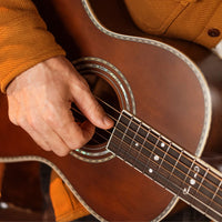 Person playing an acoustic guitar with a close-up of the hand on the fretboard.